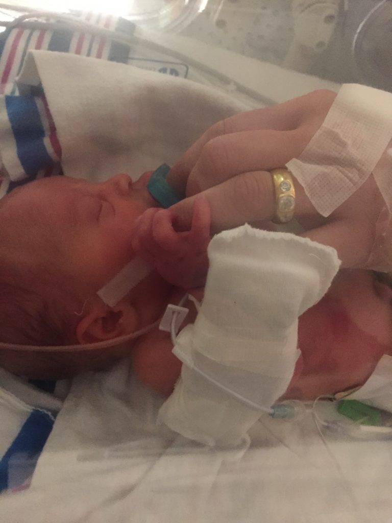 Nicu newborn holding his mother's hand.