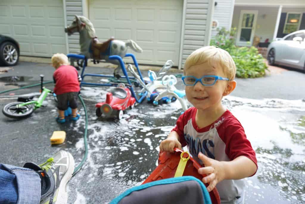 Twin toddlers washing a play horse in a driveway. Dilli Dalli Glasses