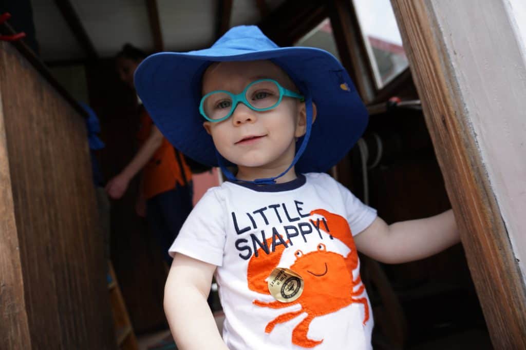 Toddler in Dill Dalli glasses standing inside a work boat.